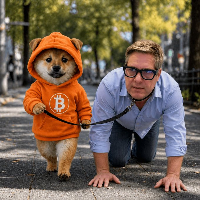 A man wearing glasses crawls on a sidewalk while being led by a Shiba Inu dog dressed in an orange Bitcoin hoodie.