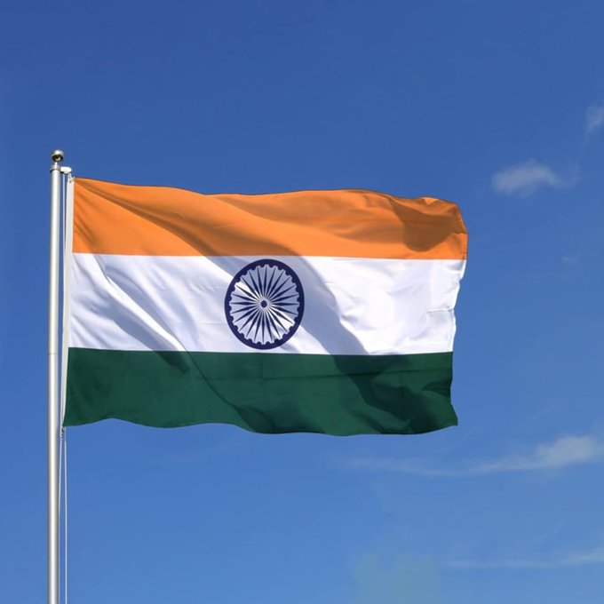 The Indian national flag, featuring saffron, white, and green horizontal stripes with the Ashoka Chakra in the center, waves against a blue sky.