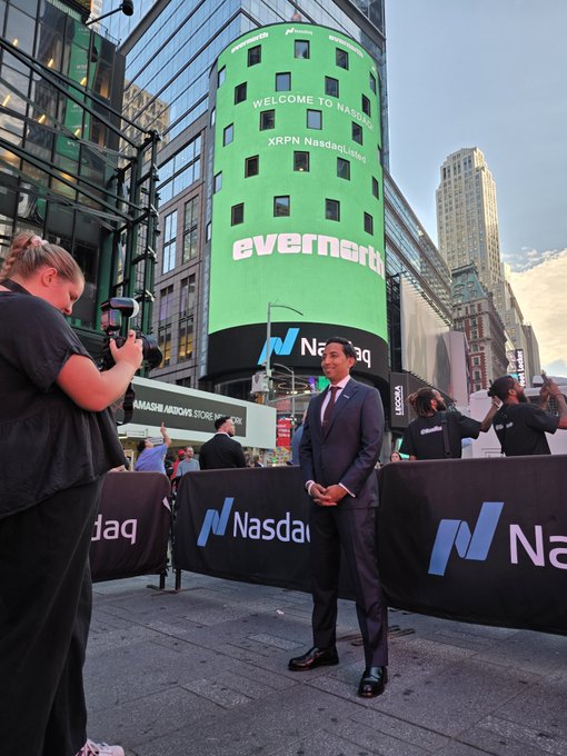 A man in a suit stands in front of the Nasdaq building during the 'everneth' XRPN Nasdaq Land event, while a photographer captures his portrait.