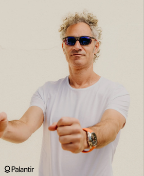 A man with curly blonde hair and dark sunglasses, wearing a white t-shirt and an orange watch, points directly at the camera, with the "Palantir" logo visible in the corner. The image accompanies a quote from Dr. Karp about seeking competent technical partners for $ZETA shareholders, emphasizing Palantir's collaborative yet independent approach to partnerships.
