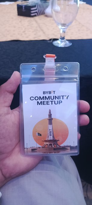 A hand holding a plastic badge holder displaying a "BYBIT COMMUNITY MEETUP" pass featuring an illustration of the Minar-e-Pakistan monument in Lahore.