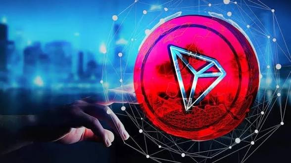 A hand reaches toward a glowing red Tron cryptocurrency logo set against a blue cityscape background with a network of connecting lines and nodes.