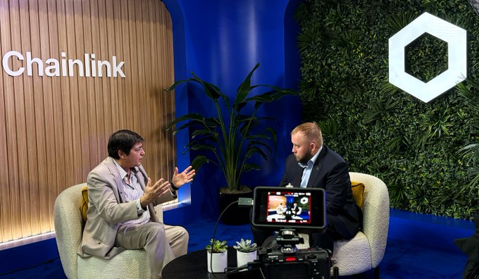 Two men, including Sergey Nazarov, engage in conversation at the Chainlink booth during Sibos 2026, with a camera setup in the foreground capturing their discussion about the DTCC Collateral AppChain and tokenized securities.