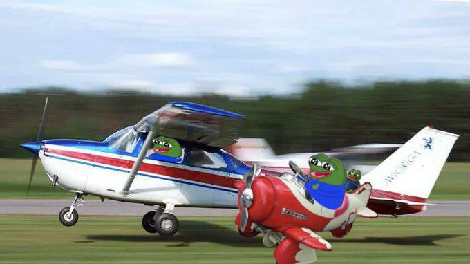 A small white, red, and blue Cessna airplane on a runway alongside a cartoon red airplane piloted by a green Pepe the Frog character.