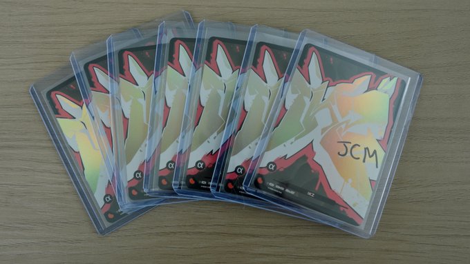 A fan of five holographic trading cards with red borders and 'JCM' signed on the top card, displayed in clear sleeves on a wooden surface.