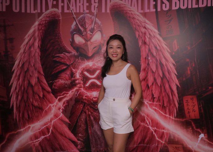 A smiling woman in a white tank top and shorts poses in front of a large promotional backdrop featuring a red winged character and text reading "UTILITIES: FLARE & ITS WALLETS BUILDER" alongside Japanese characters, tied to an IRL community event hosted by Flare Japan Group and Flare Networks.