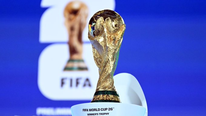 The image features a golden trophy for the FIFA World Cup, which is placed inside a white pedestal with a gold base. The trophy is positioned against a blue background, drawing attention to its significance. In the background, there are two other smaller trophies displayed on pedestals, one of them being the "Kraken & Chainlink" trophy. The post also mentions that Kraken and Chainlink have been named official partners for the FIFA World Cup, with Kraken acting as the Crypto Exchange Supporter and Chainlink serving as the prediction market partner.