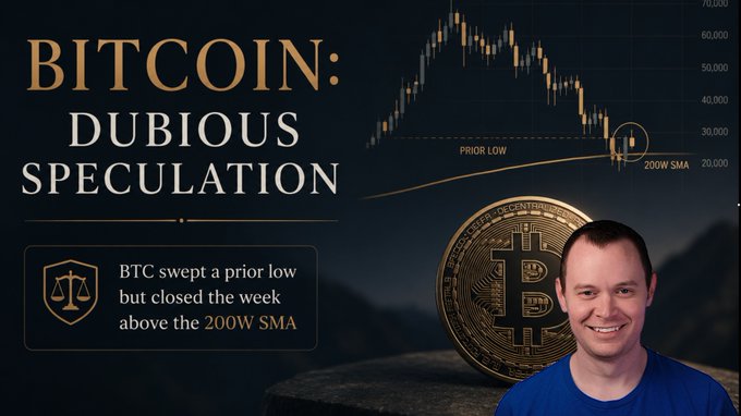 The image features a man wearing a blue shirt smiling at the camera while standing next to a mountain range. The caption of the image reads "Bitcoin: Dubious Speculation... but closed above the 200w SMA", which suggests that Bitcoin has dropped below the 200-point mark in the past week, and it is possible that it might continue to drop further until year-end.