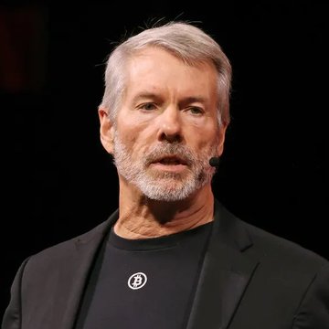 The image shows Michael Saylor, the founder and executive chairman of MicroStrategy, speaking on stage with a headset microphone, wearing a dark blazer over a black t-shirt featuring a Bitcoin (₿) logo. His appearance relates to the accompanying quote, which reflects his well-known advocacy for Bitcoin as a transformative financial instrument and his vision for significant capital flow into Bitcoin-backed credit markets.