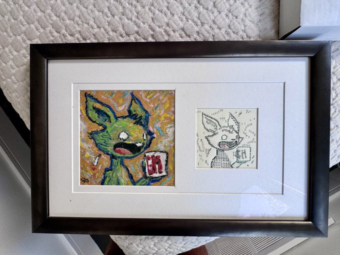 A black-framed display features a vibrant, colorful painting of a green creature holding a beer mug alongside its original black-and-white ink sketch, showcasing the creative process from concept to finished artwork.