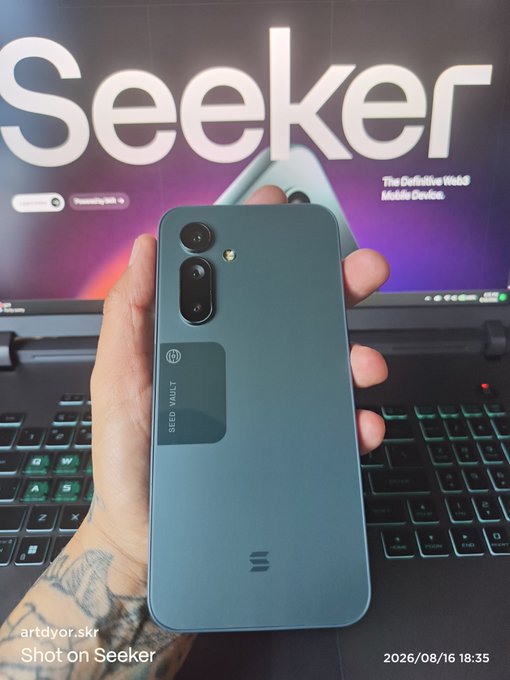 A hand holds a gray "Seeker" mobile device—branded as "The Definitive Web3 Mobile Device"—in front of a monitor displaying the Seeker logo, with a visible watermark reading "Shot on Seeker." The image showcases the Solana Seeker Android phone, tying directly to the "Solana Seeker Summer on your mobile!" theme by highlighting the device's Web3 capabilities.