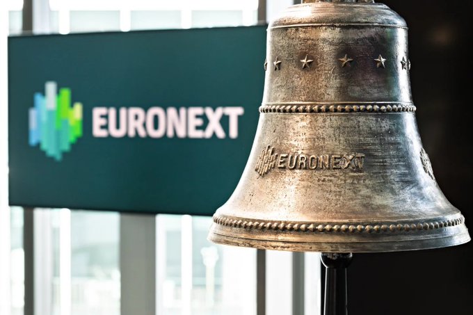 A bronze bell engraved with 'EURONEXT' and decorative beads, with the Euronext logo visible on a screen in the background.