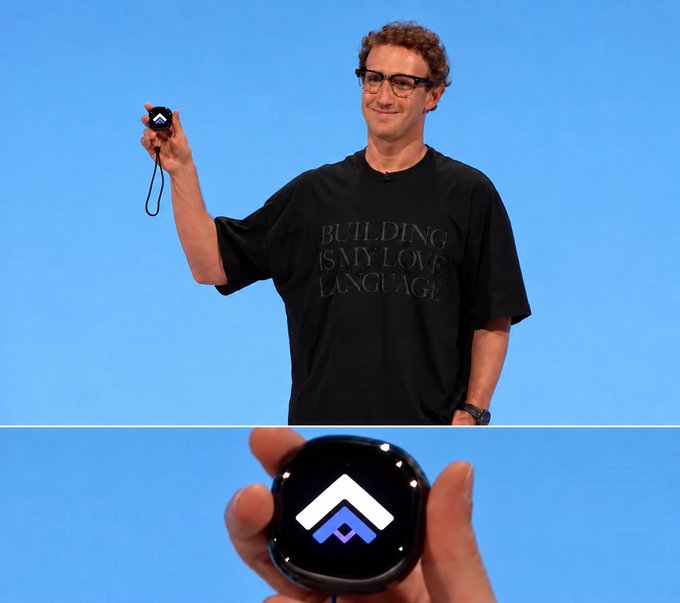 A young man with glasses wearing a black t-shirt that reads 'BUILDING IS MY LOVE LANGUAGE' stands on a stage with a blue background, holding up a small round device; a close-up below shows the device's screen displaying a blue and white upward arrow logo.