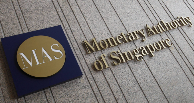The image shows the gold "MAS" logo and "Monetary Authority of Singapore" lettering mounted on a stone building facade, representing the regulator behind Singapore's new stablecoin proposal mandating 100% reserves and banning interest payments.