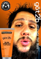 A close-up of a man with a beard holding a tube of 'got2b' hair product, with the text 'attitude for hair' and a 'GUAR' logo visible in the background.