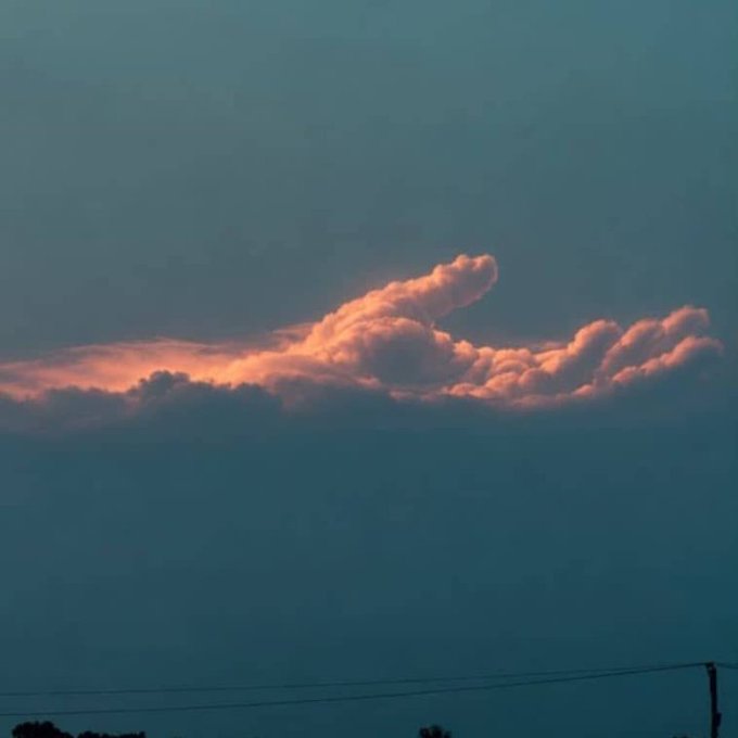A serene sky photograph at dusk or dawn, with pink and orange-tinted clouds illuminated against a blue-gray sky, with power lines visible at the bottom edge.