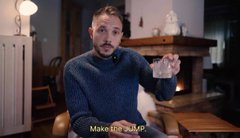 A bearded man in a blue sweater holds up a small object in a warmly lit interior with a caption reading 'Make them a MP.'