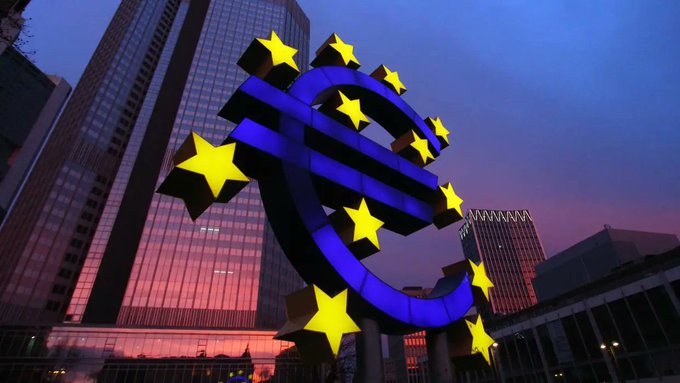 A large, illuminated Euro symbol stands in front of modern buildings at dusk, representing Europe's response to the rise of stablecoins as mentioned by ECB board member Piero Cipollone.