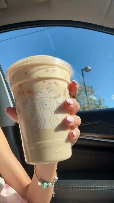 A hand with pink manicured nails and a charm bracelet holds up a Starbucks iced coffee cup inside a car. The image contrasts the post's message about financial discipline and self-custody with the relatable everyday luxury of a coffee run, suggesting that true wealth-building ("owning your keys") allows you to enjoy life's simple pleasures without reckless speculation.