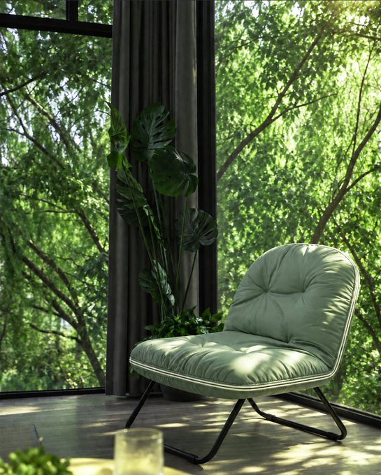 A green tufted lounge chair sits next to a window with a view of lush green trees, with a potted plant in the corner.