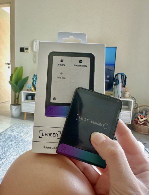 A hand holds a black "Ledger" hardware wallet displaying "TRUST YOURSELF" on its screen, with the matching "Solana Limited" edition box in the background. The image emphasizes the importance of secure cold storage for crypto, especially in light of the recent vulnerability that led to the theft of nearly 600 BTC from COLDCARD devices.