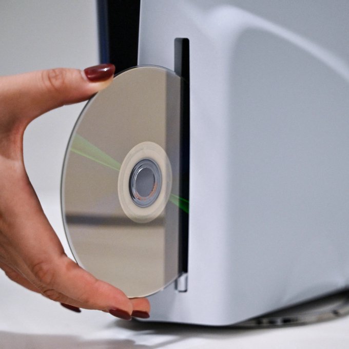 A hand with dark red nail polish inserts a reflective disc into a silver optical drive. The image humorously illustrates the post's satirical claim by juxtaposing vintage media technology with modern Bitcoin self-custody branding, though no specific text, numbers, or tickers are visible in the image itself.