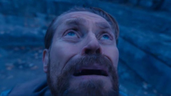 A close-up of a man with a beard looking upwards with a terrified expression in a dimly lit, cool-toned setting.