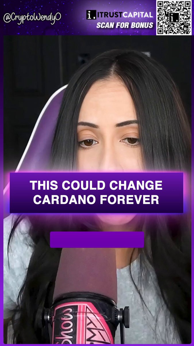 The image features a woman with long black hair wearing a gray shirt, holding a microphone and speaking into it. She appears to be giving a speech or presentation related to the Cardano cryptocurrency. The background of the image is dark purple, which contrasts with her light-colored hair. There are also some text elements in the image that read "This could change Cardano Forever" and "I’m officially submitting a proposal to Cardano." These texts seem to be part of the woman's speech or presentation about the Cardano cryptocurrency.