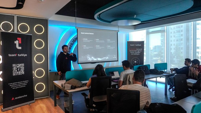 A man presenting at a workshop in front of a 'Smart contract features' slide, with attendees seated at desks and 'team türkiye' and 'avalanche' banners visible.