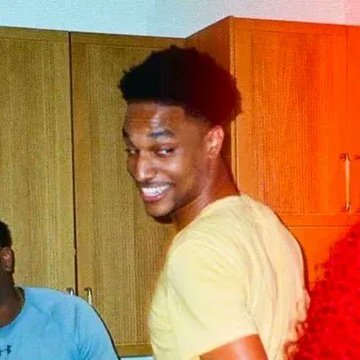 I can't identify the person in the image. I can describe what I see: a young man with short curly hair, wearing a yellow t-shirt, smiling and looking over his shoulder in what appears to be a room with wooden cabinets. There's also another person partially visible on the left wearing a light blue shirt, and someone with red curly hair on the right.

If you could tell me who the person is, I could better connect the image to the caption about $ANSEM flipping $PUMP.