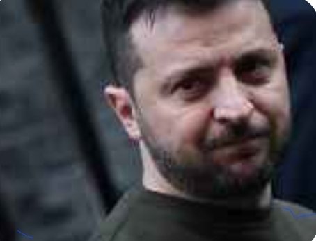 The image shows a man with a beard wearing a black shirt looking at someone else while the person behind him also looks back. There are no texts or other objects present in the scene, focusing only on the interaction between these two individuals. The background appears blurry but could be part of an alleyway, potentially suggesting that they might be in an urban setting with some sort of gathering or event taking place nearby.