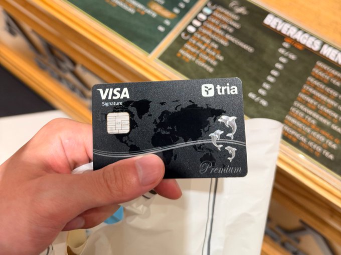 The image shows a person holding up a black Visa card, which has a map printed on it. The text on the card indicates that it is a "Premium" card issued by Tria. However, there are no other details about the card or its features in the image.