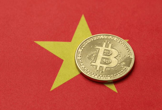 A physical gold Bitcoin coin rests on a red surface featuring a large yellow star, resembling the flag of Vietnam.