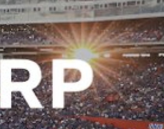 The image displays large white "RP" letters (likely cut off from "XRP") overlaid on a sunburst effect, set against a backdrop of a packed stadium with crowds in the stands. The grand, sunlit stadium setting visually amplifies the post's reference to #XRP, suggesting a triumphant or monumental moment for the cryptocurrency.
