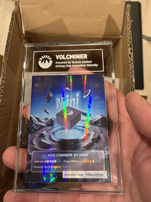 A hand holds a holographic "Volcminer D1 Mini" card over an open shipping box, displaying specs including a 500 GH/s hashrate, ~225W power efficiency, and an activation code "FF62SJOPHM" — offered free in the post to anyone who wants to claim the mining chip from Volcminer (Powered by Tecvia Limited).