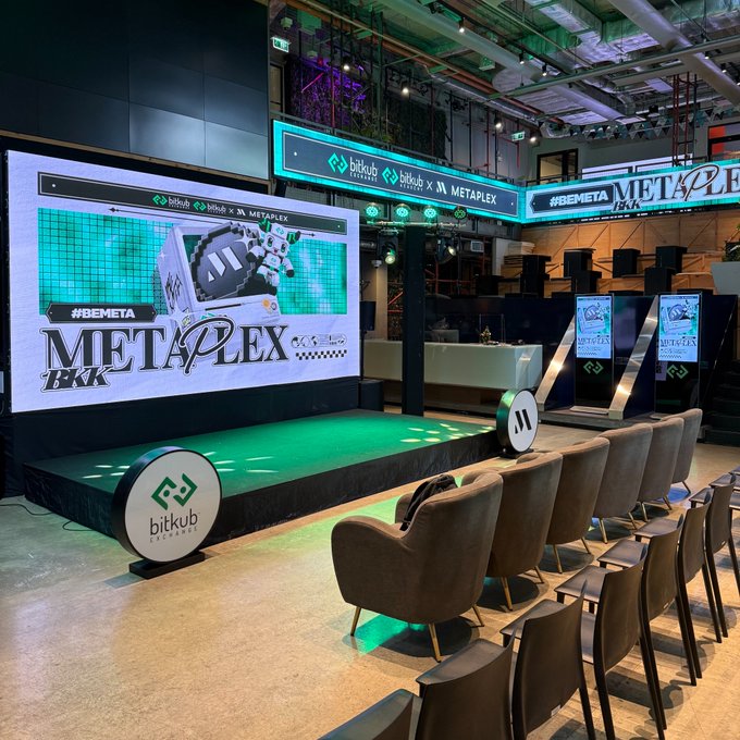 An empty event space featuring a stage with the "BEMETA METAPLEX BKK" logo, co-hosted by Bitkub Exchange, with large LED screens and rows of chairs arranged for an audience.