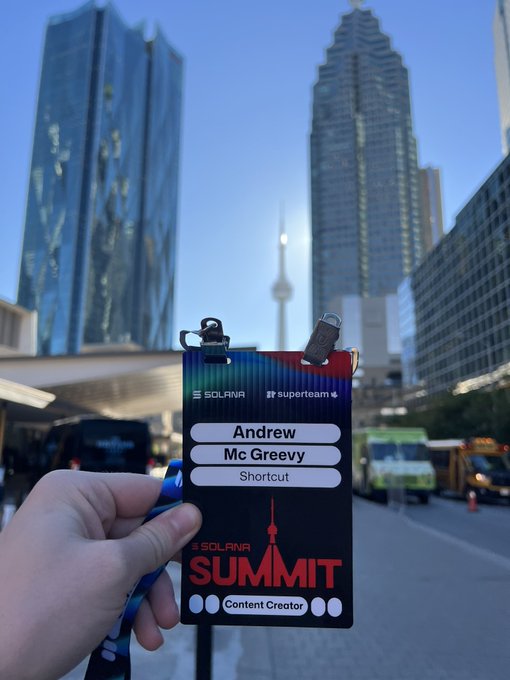A hand holds a 'Solana Summit' Content Creator badge for 'Andrew Mc Greevy' with 'Shortcut' company branding, set against a Toronto city backdrop featuring the CN Tower.