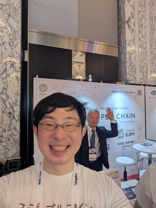 A man in a Simplex t-shirt takes a selfie while another man in a suit waves in the background at a "PE CHAIN" promotional booth, which advertises "Stablecoin EJPY" with "6,000 on First 5000+" and "11 → 1000+ NPCs Trusted Validators" text, tying into the post about someone working on stablecoins.