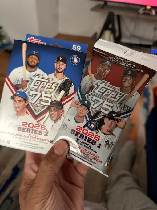 A hand holds two unopened 2026 Topps Series 1 and Series 2 baseball card value packs featuring players like Ohtani, Judge, and Skenes.