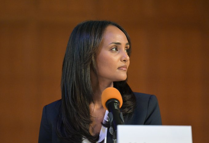 This image shows Melat Kiros at a podium with an orange microphone, fitting the accompanying post about her winning the CO-01 Democratic primary with a 99% chance projected by Polymarket.