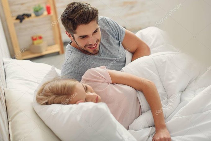 A stock-photo scene shows a man and a woman lying under white bedding in a bright bedroom, both smiling or laughing. Faint diagonal watermarks read “depositphotos.”