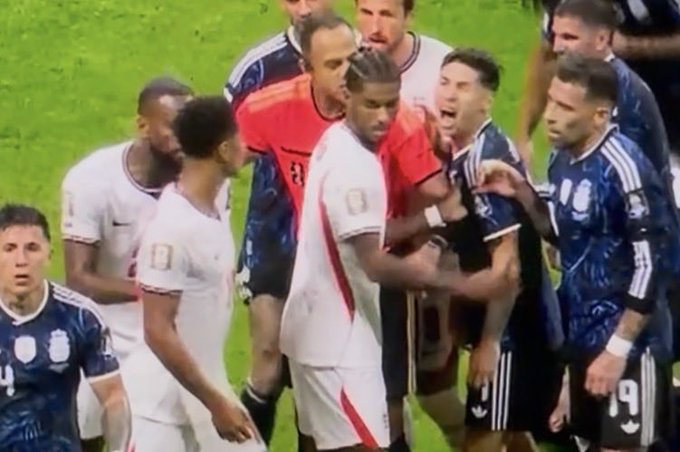 Soccer players from opposing teams, including one wearing a white jersey with "19" visible, engage in a heated confrontation on the field, appearing to reflect the on-pitch tension referenced in the post about Gonzalo Montiel and Marcus Rashford.