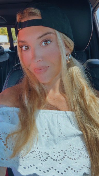 A young blonde woman wearing a black backwards cap and a white eyelet off-shoulder top takes a selfie inside a car, posing with a soft smile. The image's casual, upbeat vibe complements the enthusiastic "GO CARDS" celebration paired with the Polymarket partner tag.