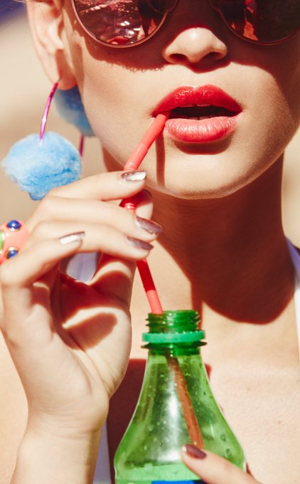The image features a woman with red lipstick, wearing sunglasses and holding a green bottle of soda while drinking from it. The photo has been edited or altered to include a watermark that reads "@Space_Sprockets superrare.com/artwork/eth/0x". This watermark suggests the image is part of a collection or series related to the artist or brand @Space_Sprockets, possibly for advertising purposes.
