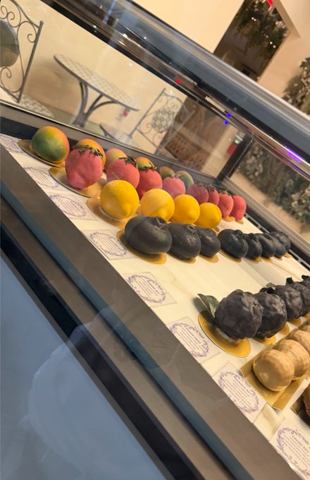 Display case showing rows of decorative marzipan fruits and vegetables, including lemons, strawberries, and eggplants.