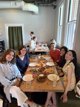 A group of women enjoys a lively brunch together at a long table filled with shared plates, drinks, and food, smiling for the camera in a bright restaurant setting. The gathering reflects the post's description of a stylish San Francisco brunch with women in AI, sponsored by @near_ai.