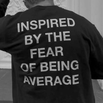 A black-and-white photo shows the back of a person wearing a t-shirt that reads "INSPIRED BY THE FEAR OF BEING AVERAGE." The bold motivational message complements the trading week's wish, capturing the drive needed to succeed and stand out in the markets.