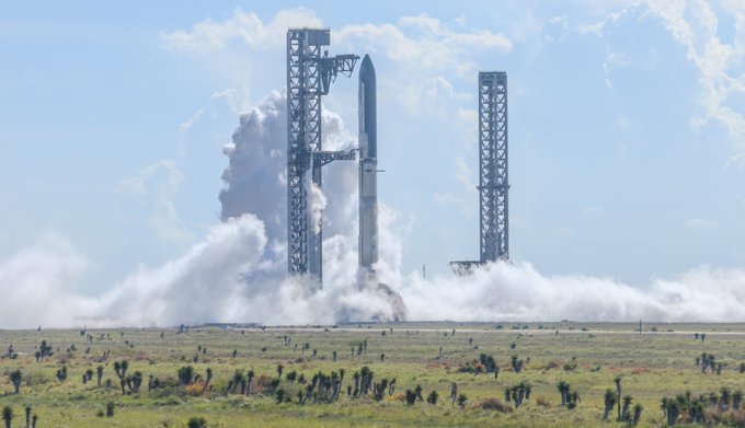 A SpaceX Starship rocket lifting off from a launch pad, producing large clouds of smoke and steam against a blue sky with scattered clouds.