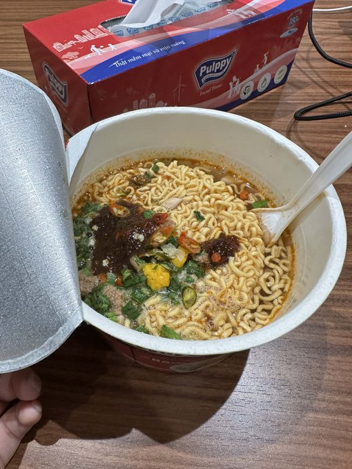 A steaming cup of noodle soup garnished with vegetables and herbs in a container. Above the cup is a red and blue box of facial tissue. The soup appears to be "luxurious" and may indicate $500 as a monetary goal the individual is hoping to reach.