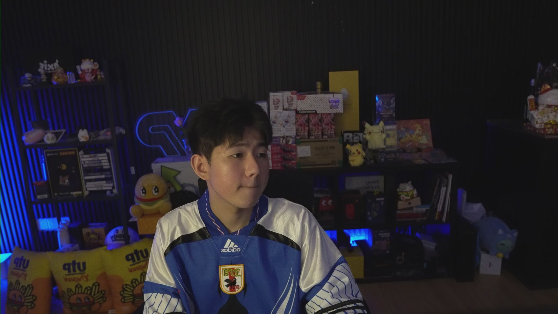 The image features a young man wearing a blue and white jersey with a red dragon emblem, sitting at a desk surrounded by various items such as books, toys, and other objects. The background shows a black wall with a neon sign that reads "@Predictdotfun $2M World Cup". The post suggests that the person should focus on winning the @Predictdotfun $2M World Cup in order to achieve their goal.